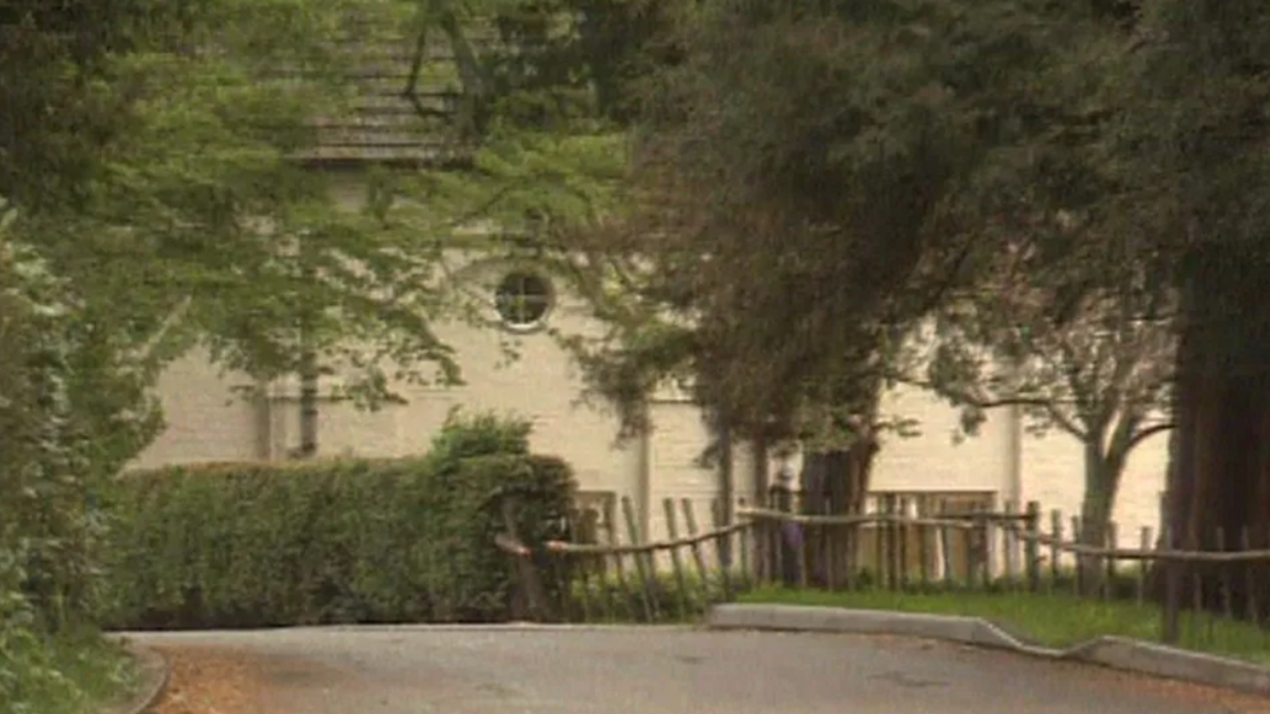 Former Rhydd Court School in Hanley Castle, showing a white building covered by bushes and trees