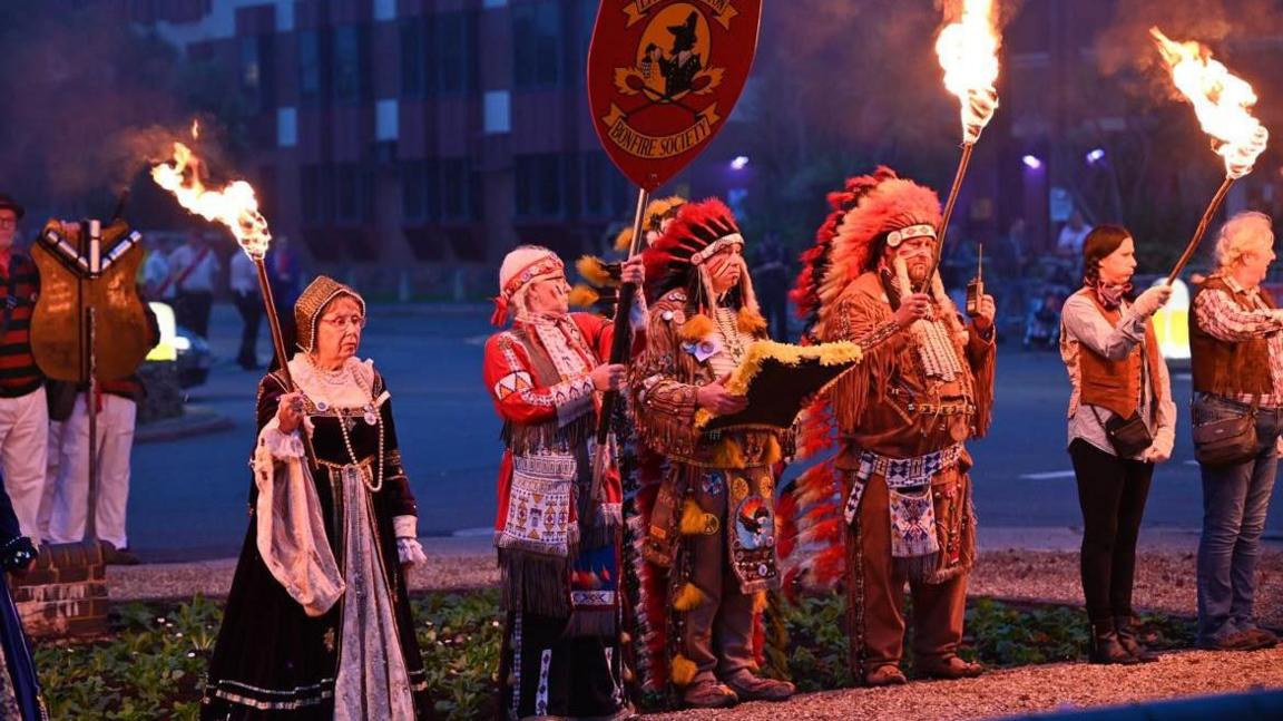 A row of Littlehampton Bonfire Society members holding lit torches and dressed in fancy dress costumes