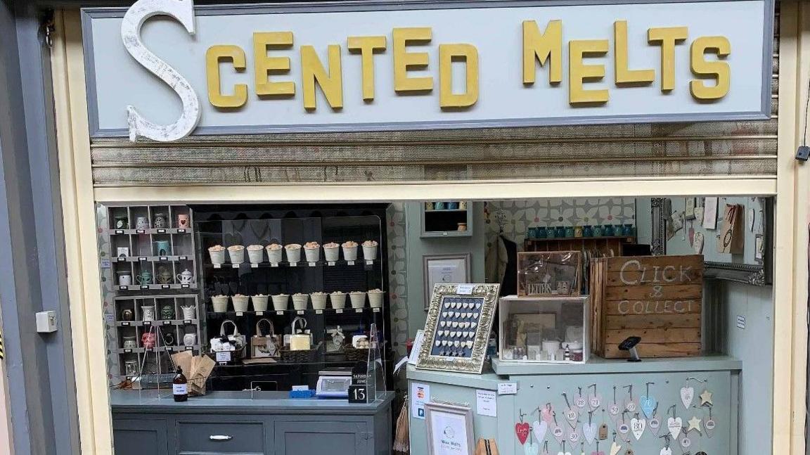 The Scented Melts shop front. It is grey with Scented Melts written in gold. There are a number of jars on a shelf behind the grey counter.