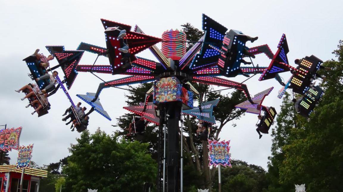 A fairground ride called Supertrooper swings people around mid-air. It has lots of multi-coloured lights.