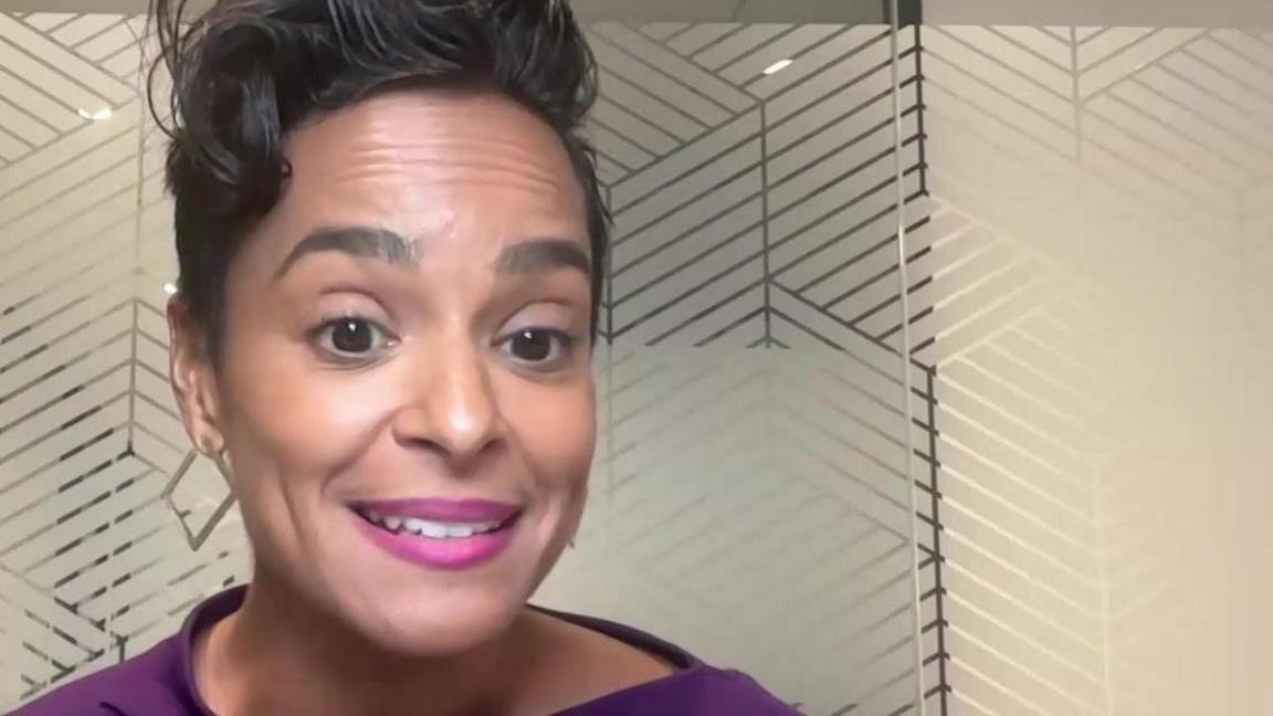 Jasmine smiles to camera - she is wearing a purple top. She is in an office. 