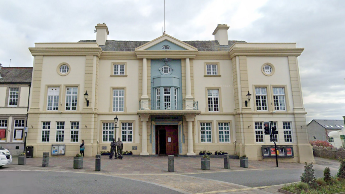 A stately white and light blue building. It has columns running down the facade with double wooden doors at the entrance