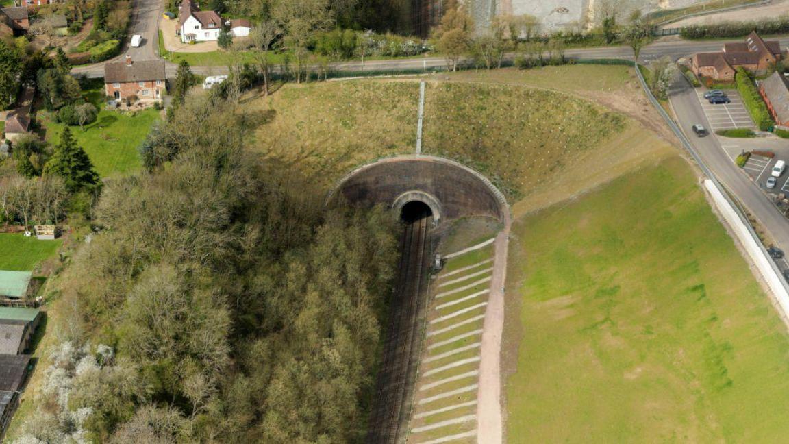 A view of one side of the tunnel in April 2021 after the cutting has been restored and the ground seeded. The land is covered in light green shoots and work has been done nearer the track.