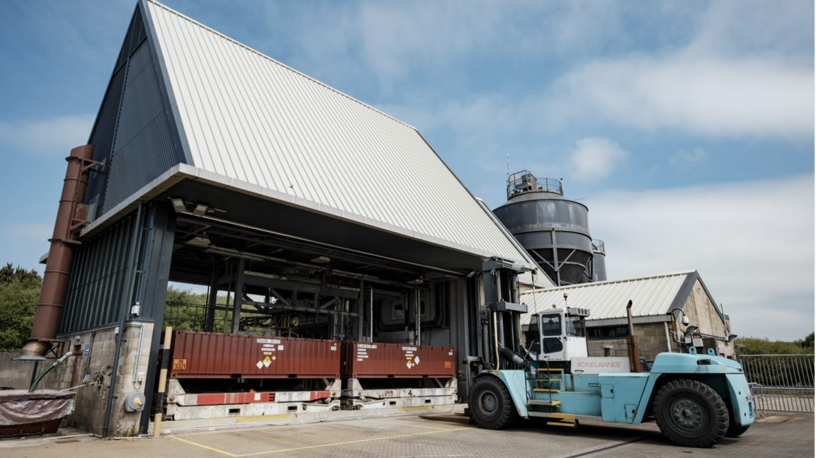 A forklift struck in front of a metal shed structure where two containers are stored.