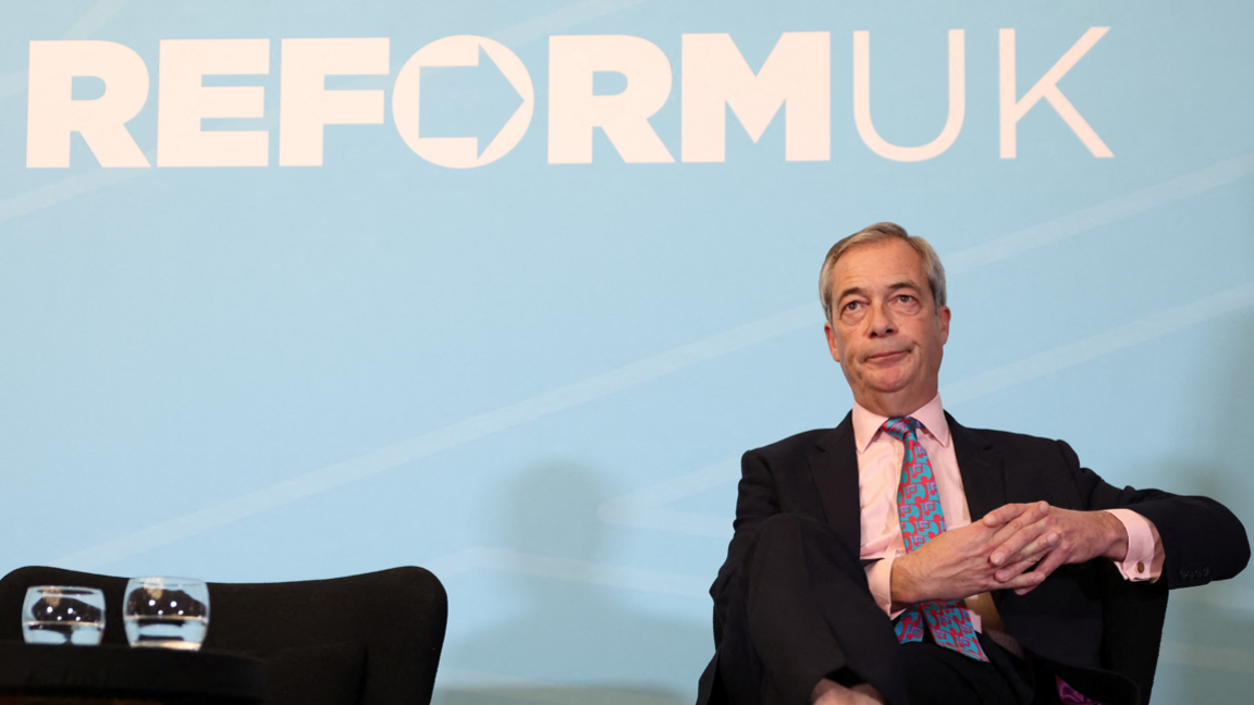 MP Nigel Farage sitting in front of a blue Reform sign