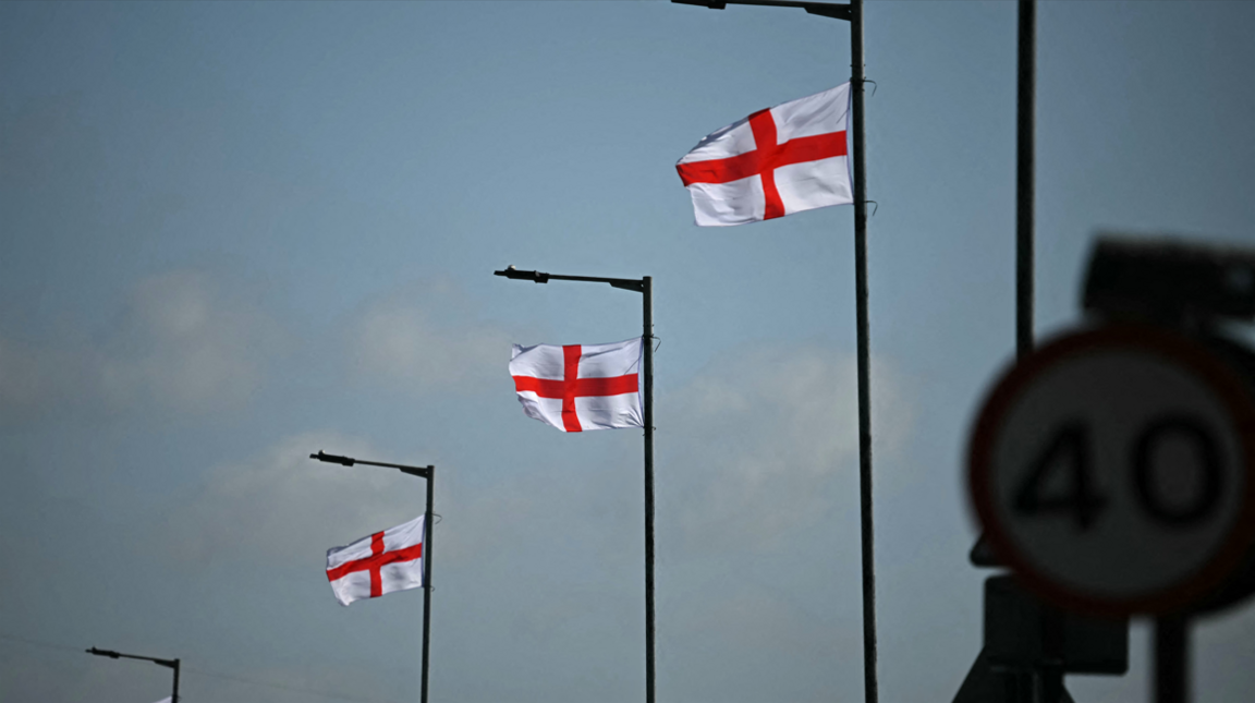 Three street lamps with St George's crosses hanging near the tops against a blue sky with white clounds. In the foreground, a 40mph speed limit sign.