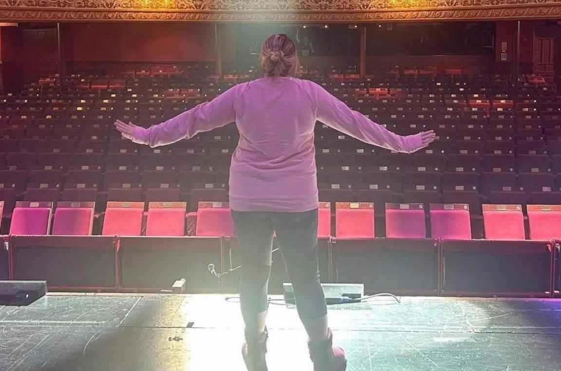 A woman in a pink top has her back to the camera and is facing the empty seats.