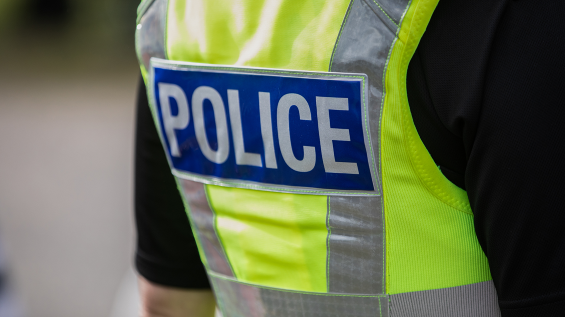 The back of a police officer wearing a hi-vis police vest and black t-shirt.