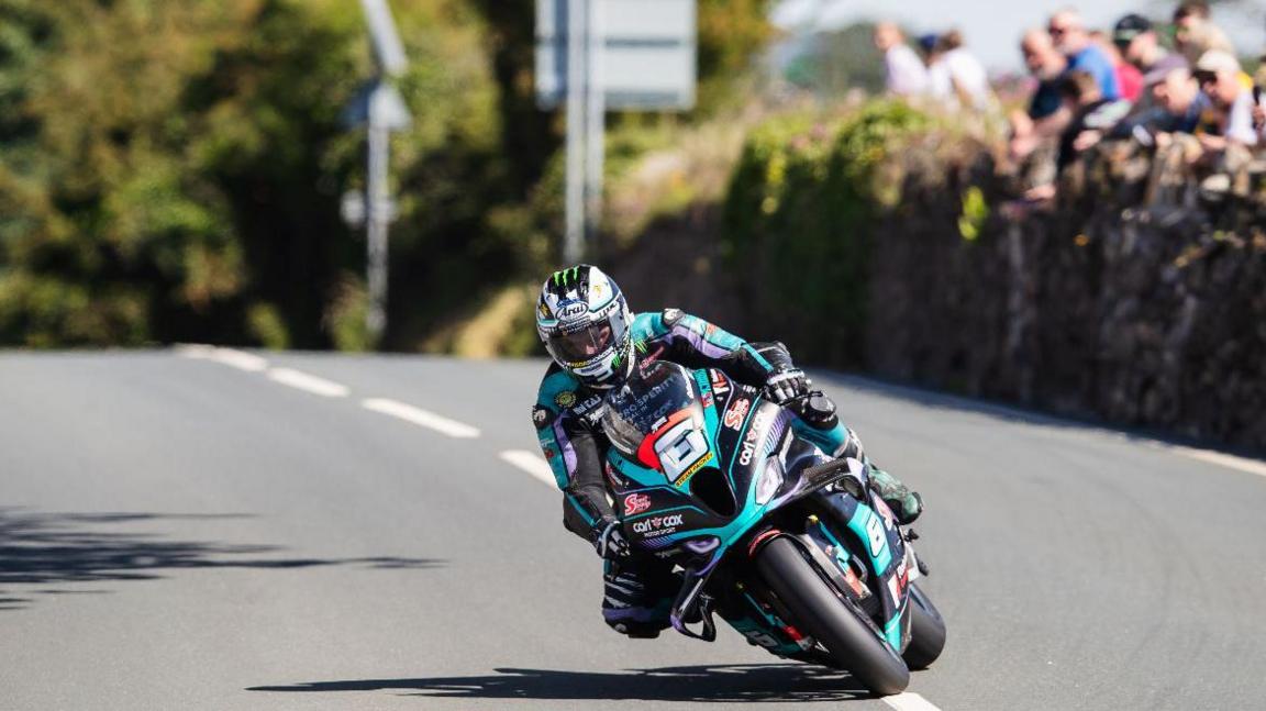 Michael Dunlop leaning over on the track with spectators watching on from the right.