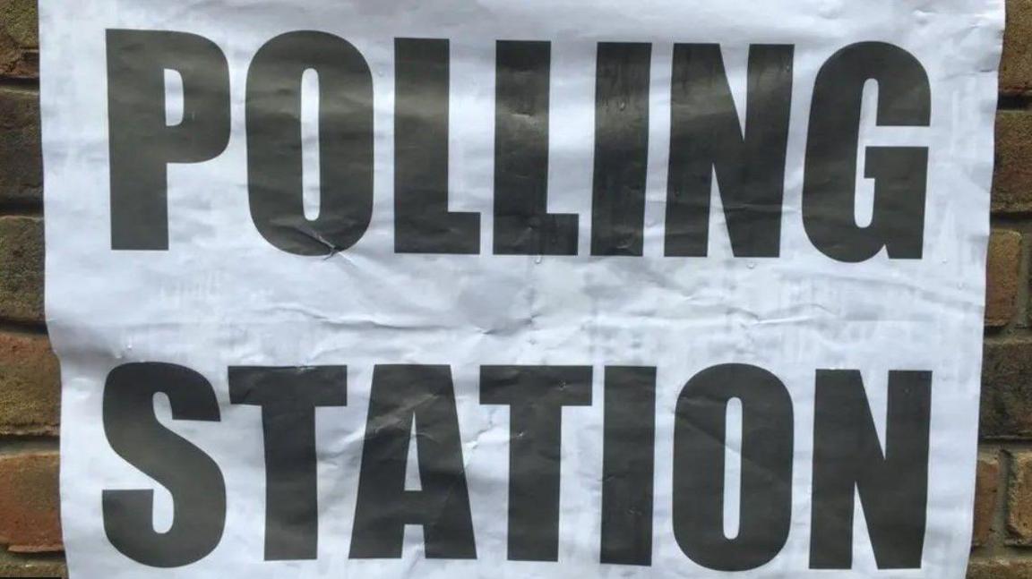 A black and white sign saying polling station fixed to a brick wall.