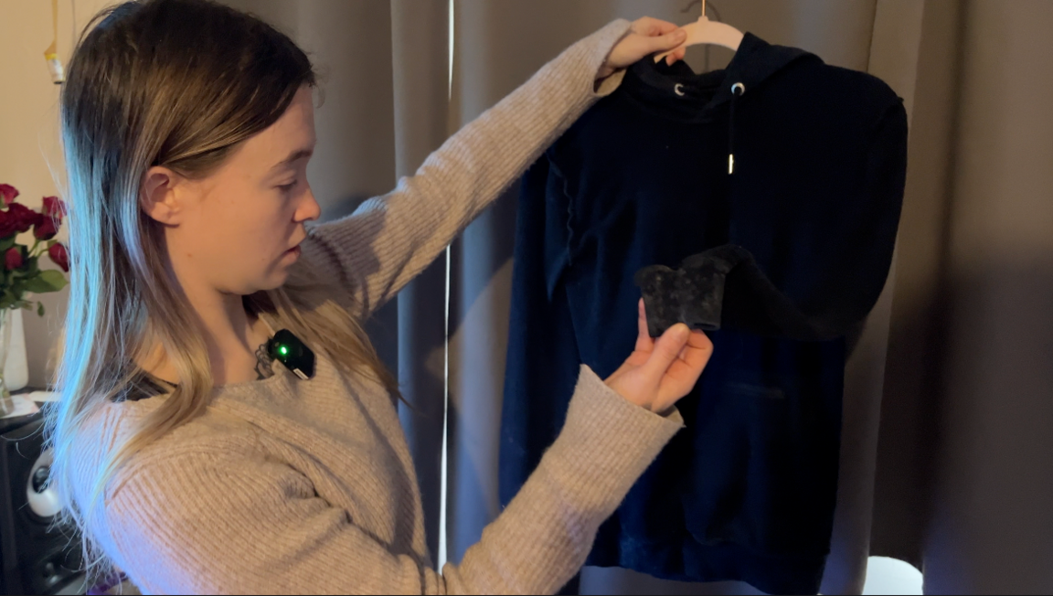 A woman wearing a grey jumper with long straight hair holds up a hoodie which has a mouldy sleeve.