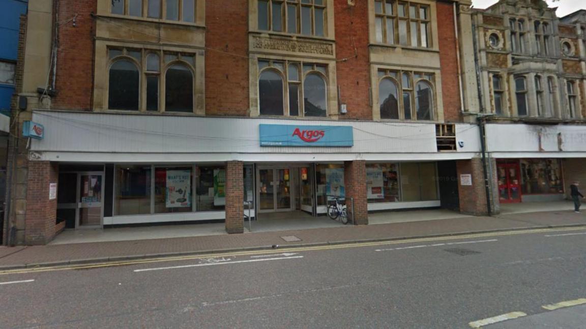 A three-storey brick building with a blue "Argos" sign on the front looking out onto a main road.