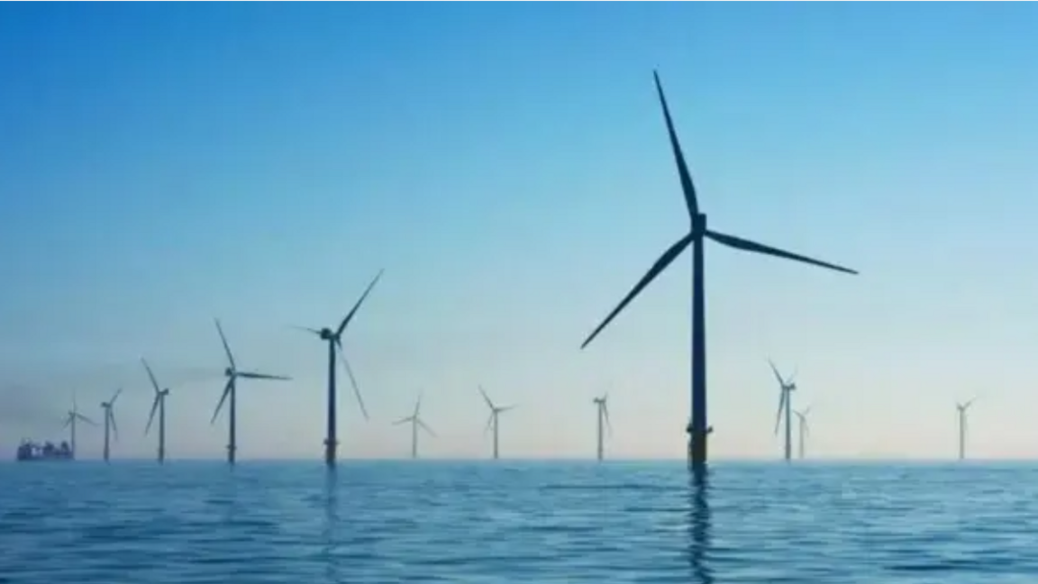 A number of wind-turbines emerging from the ocean surface against a blue sky