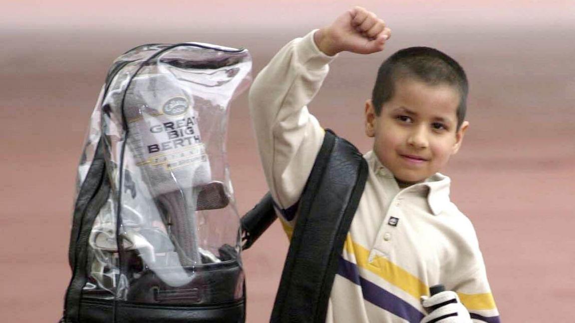 a picture of Aaron Rai as a child with a big back slung over his shoulder and his fist in the air