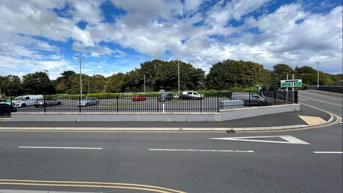 The exterior of the Bowl car park, black railings stand on its exterior. It sits next to two empty roads. There are about a dozen cars parked up in the car park.