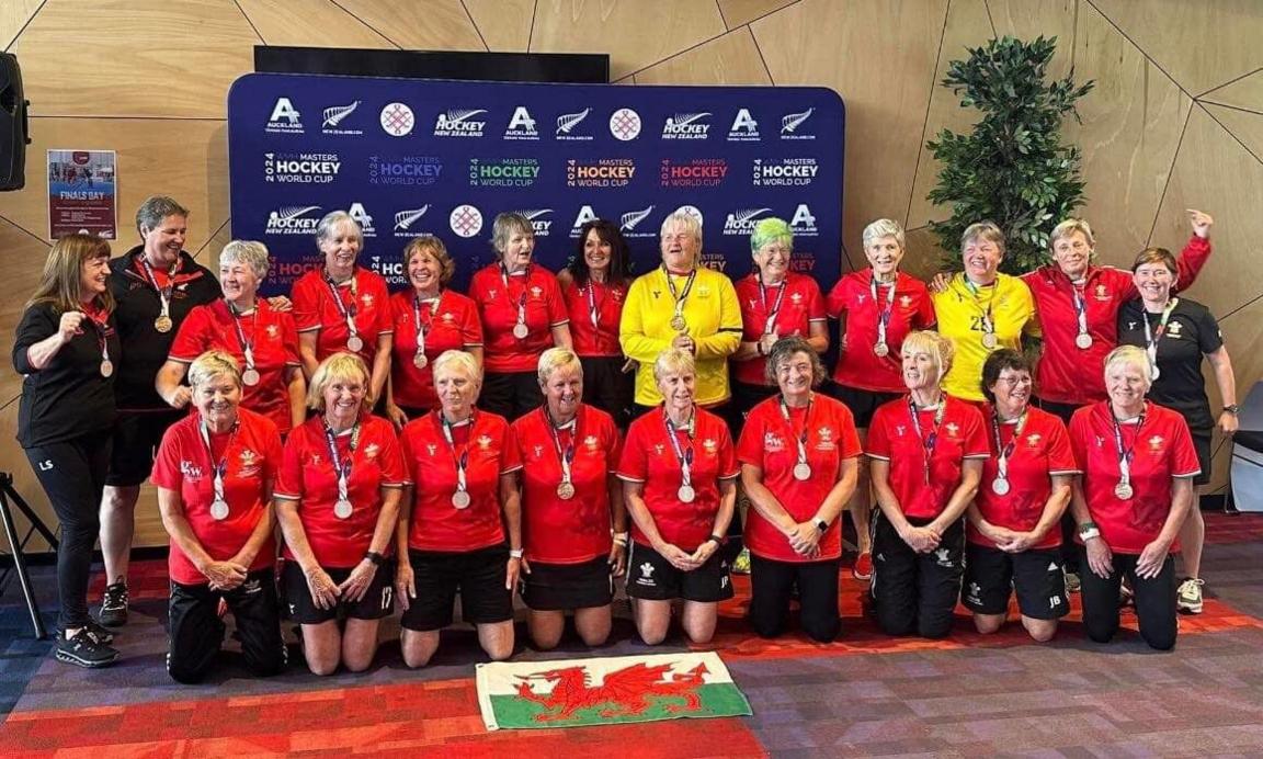 Picture of the over 65s Hockey team, wearing medals around their necks and all in their red welsh jersey tops. 