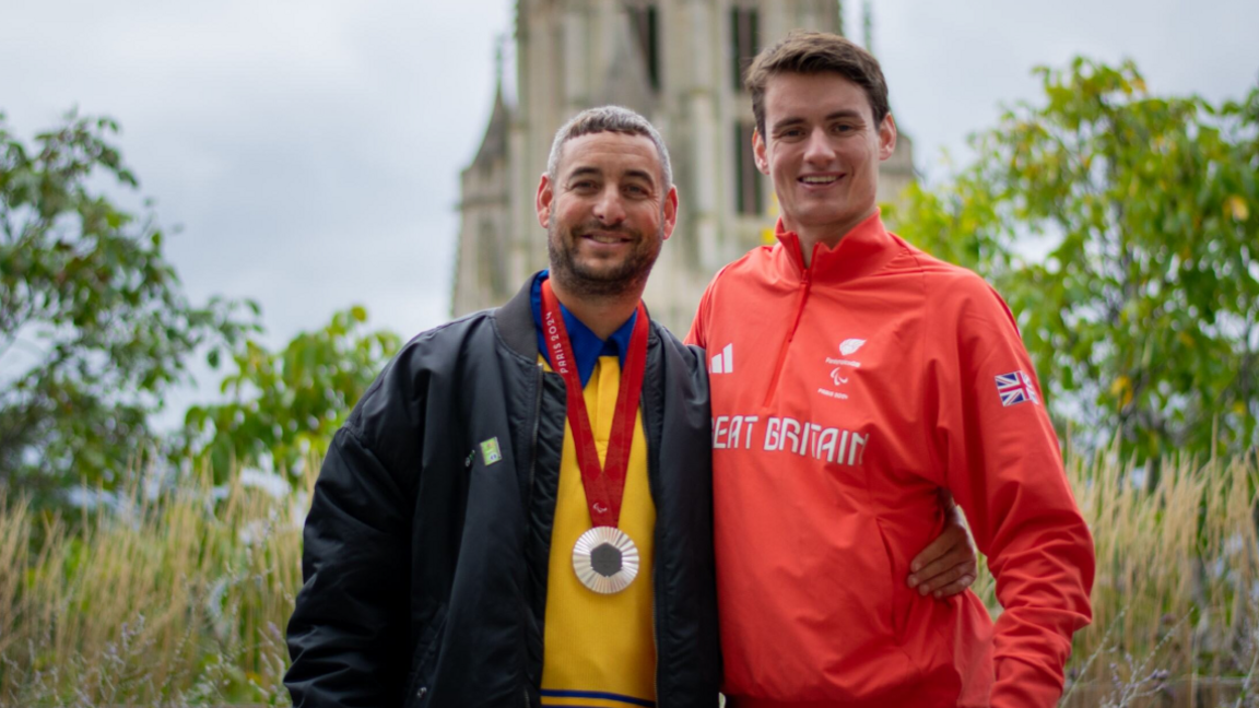 Matt Paine, wearing the Paris silver medal, standing with his arm around Mr Bethell, who is wearing his Team GB red tracksuit top, with the Wills Memorial building out of focus in the background