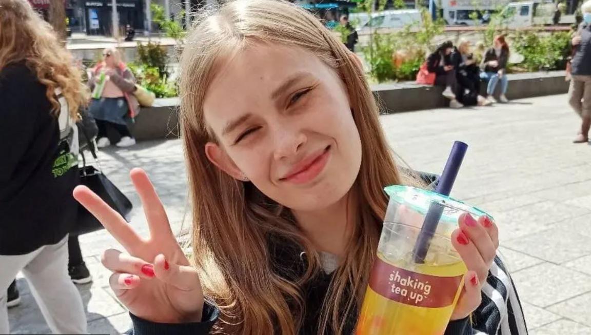 Image of Rhianan holding up a bubble tea and giving a peace sign. She has blonde hair. 