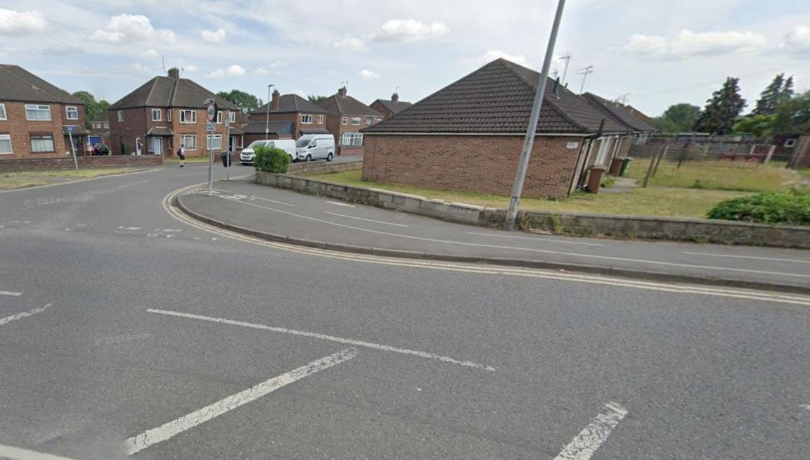 View of the junction road layout showing  bend, yellow lines and various street furniture. A number of houses can be seen in the background