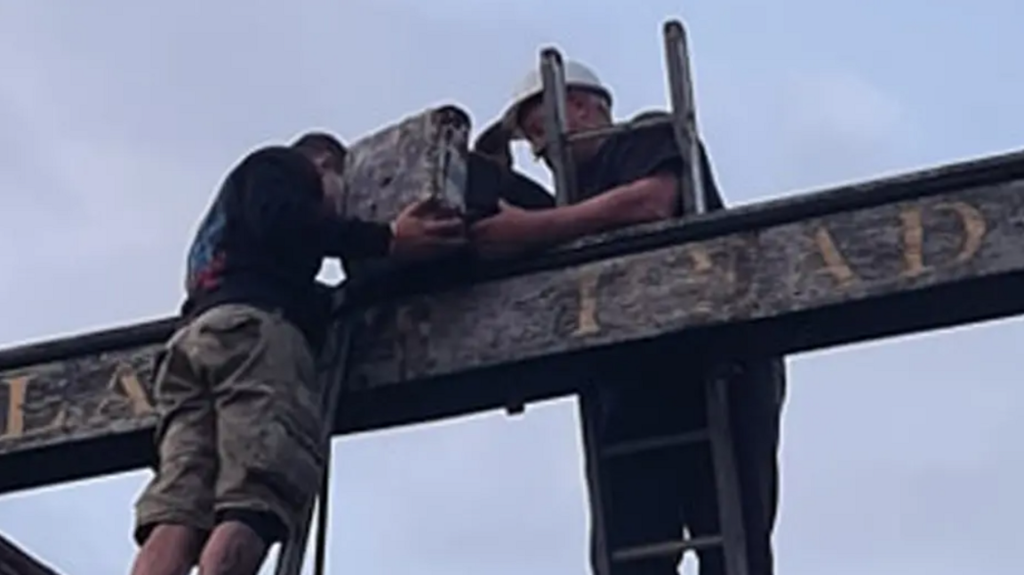 Two men on ladders removing the sculpture