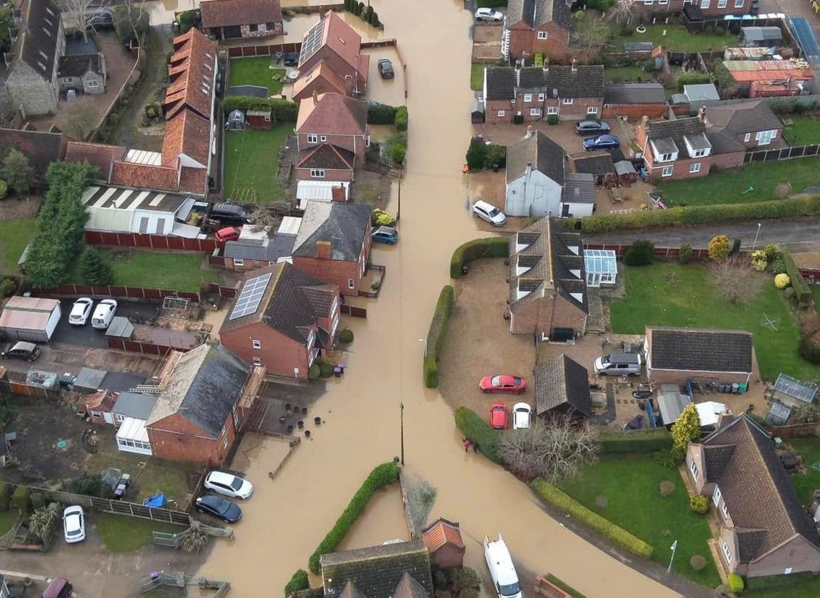 An aerial view of a residential street with rows of homes on either side inundated with brown flood water