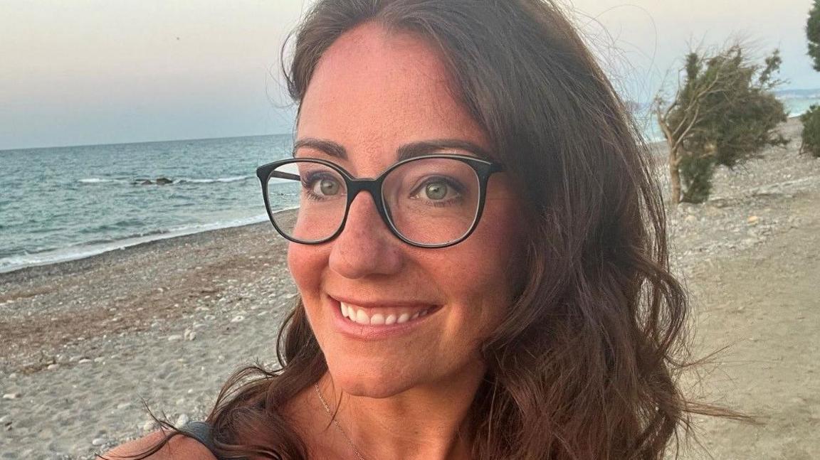 Samantha Gelder stood on a beach wearing glasses 