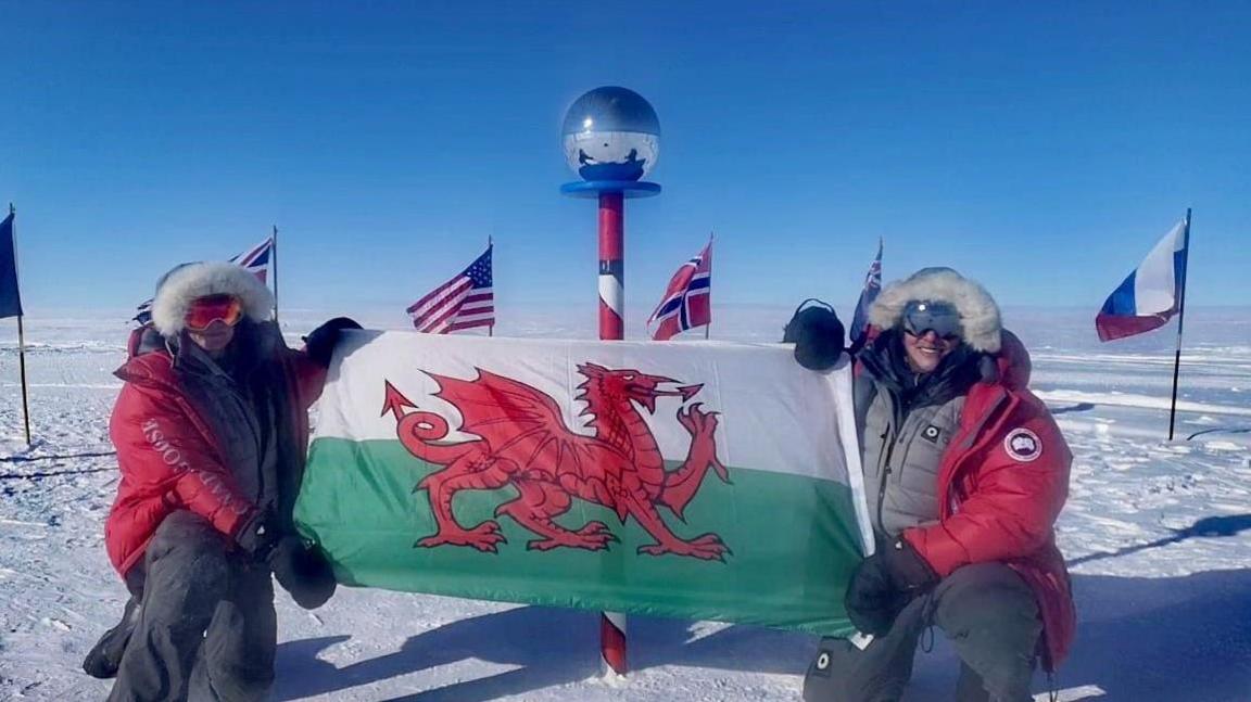 Georgina Gilbert and Rebecca Openshaw-Rowe posing with a Welsh flag at the ceremonial South Pole.