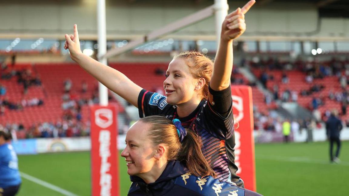 Wigan Warriors player Grace Banks holds arms aloft as she is carried by a teammate after beating St Helens.