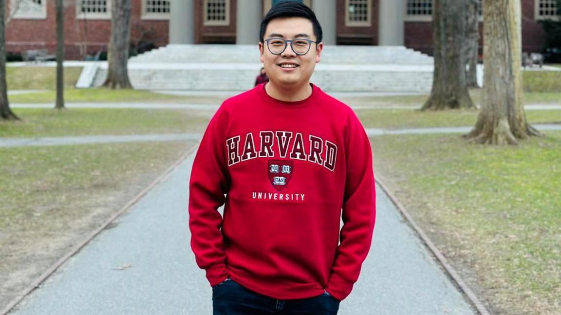 Jiang Fangzhou in a red Harvard jumper poses for a photo on campus