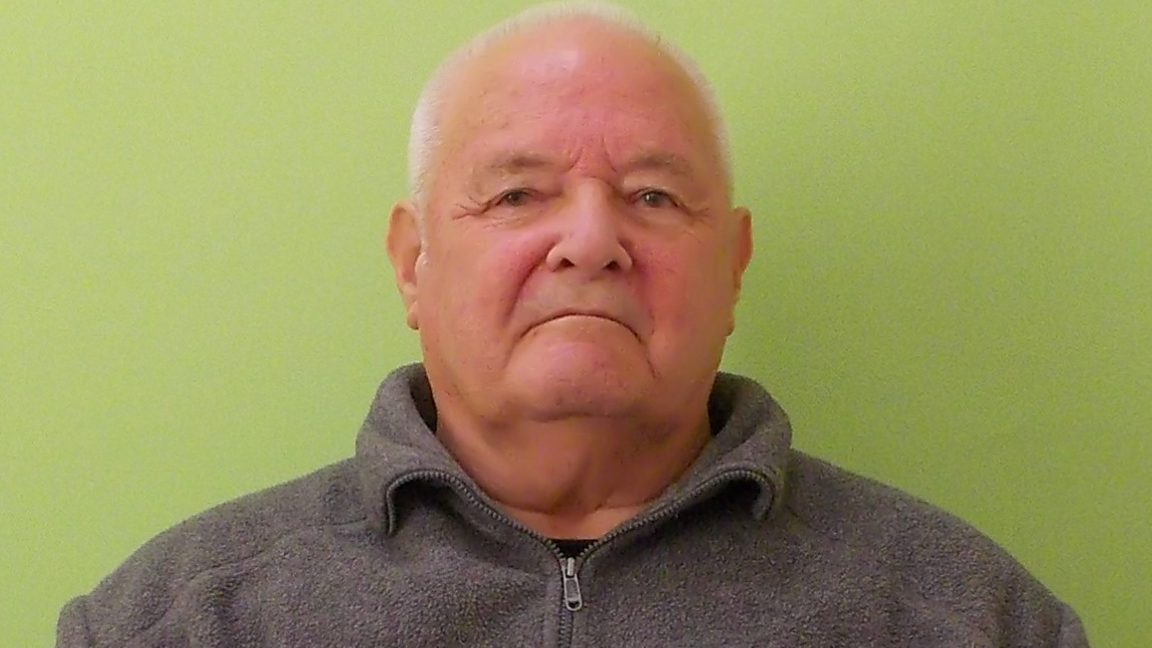 Michael Cotterill steadily looks at the camera with a lime green screen behind him. He has short white hair and is wearing a grey fleece.