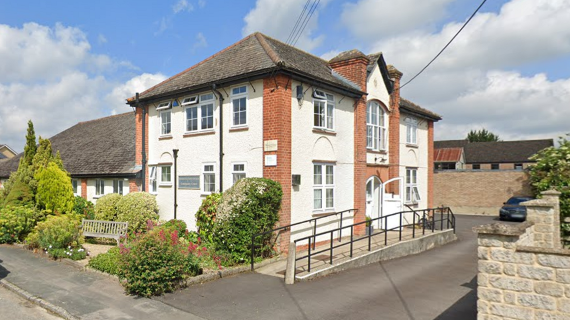 A large white two-storey house with a bench outside and a wheelchair ramp leading to a side door.