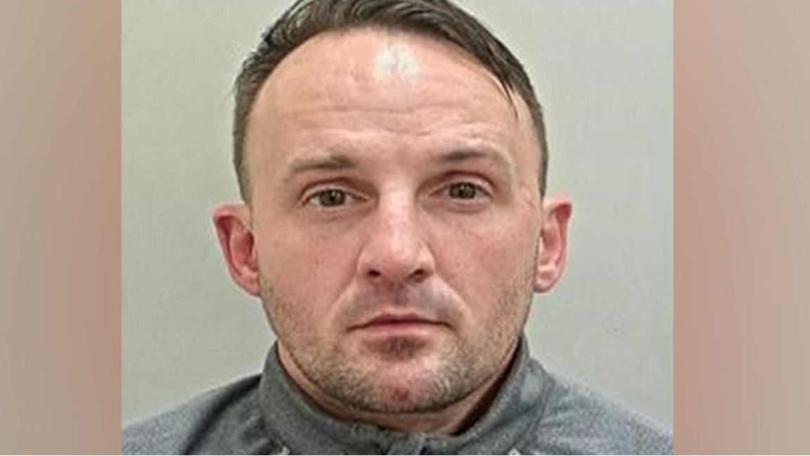 Micheal Hesketh, with short brown hair and stubble, looks impassively towards the camera in his police mugshot.