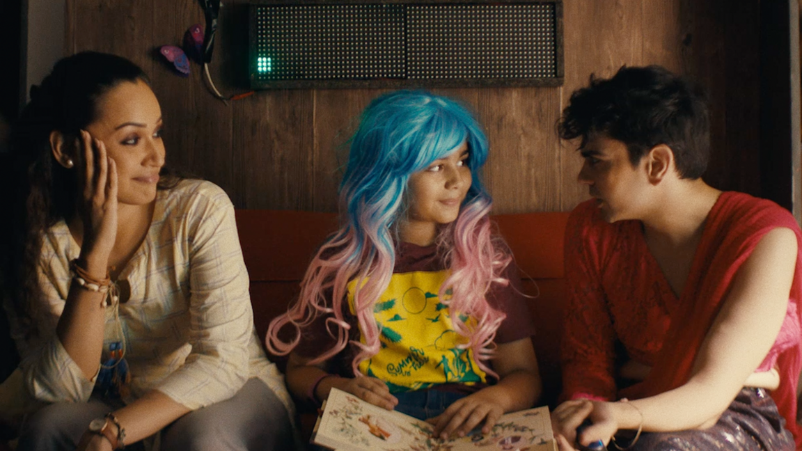 A girl in a wig smiles at a boy next to her while a woman looks on