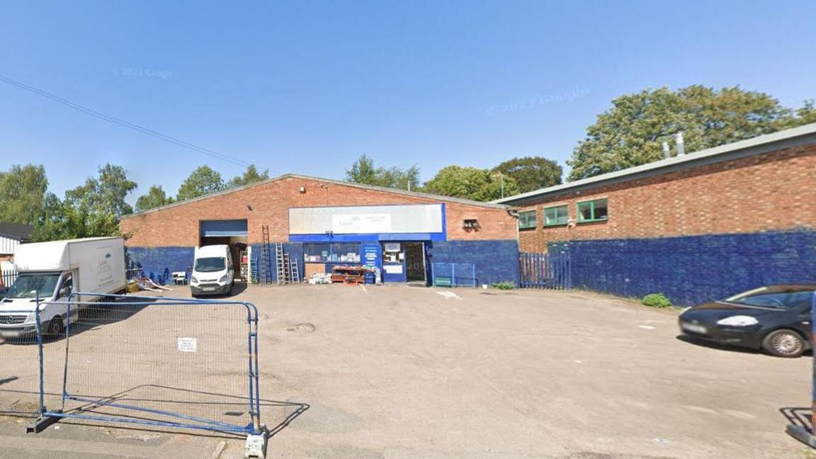 Image of Love Coventry Charity Shop with signs on a building in the background and vehicles on the left and right