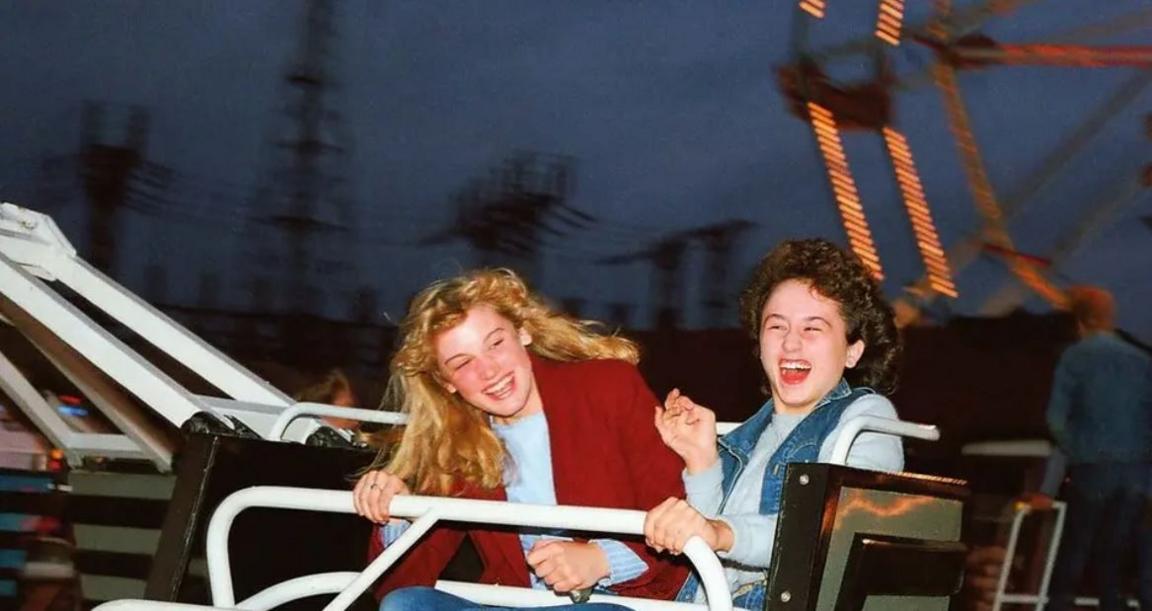 Two girls smile broadly as they enjoy a fairground ride.