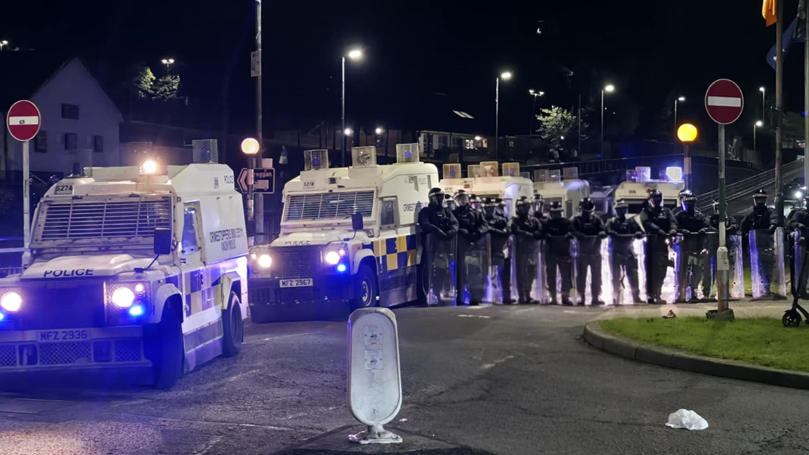 Shows white police Land Rovers with more than a dozen riot police in black and wearing helmets and carrying transparent shields