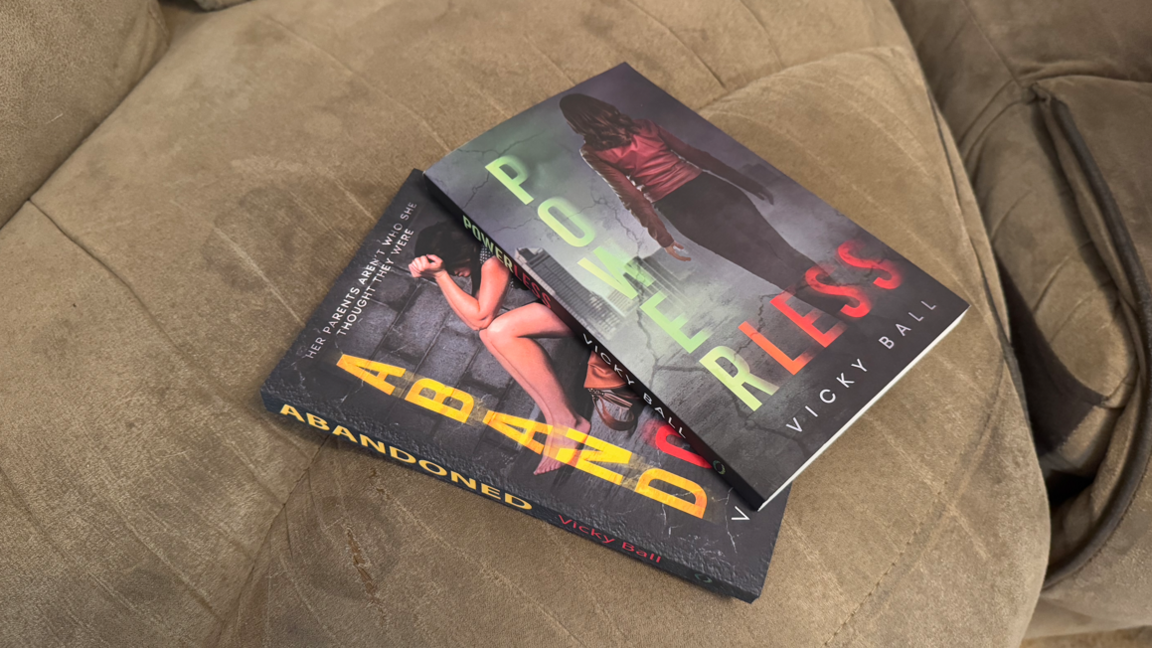 Two copies of the author's books laid on top of each other on a brown sofa.