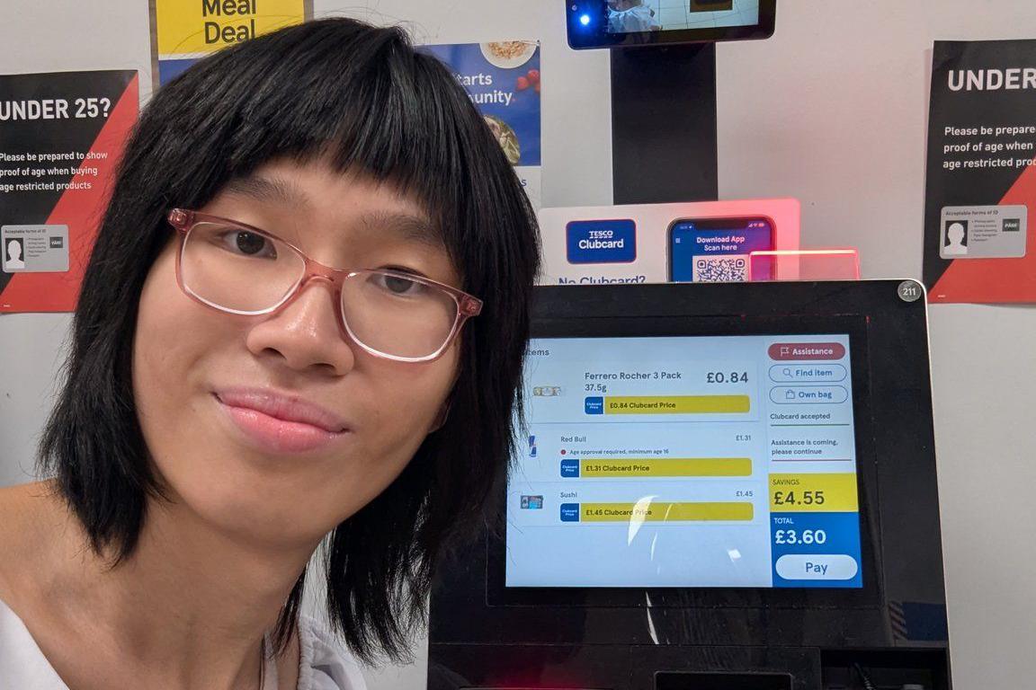 Kristina with short straight black hair and glasses with her face close to a Tesco self service machine taking a selfie to show the price for a meal deal as £3.60 before the price increase