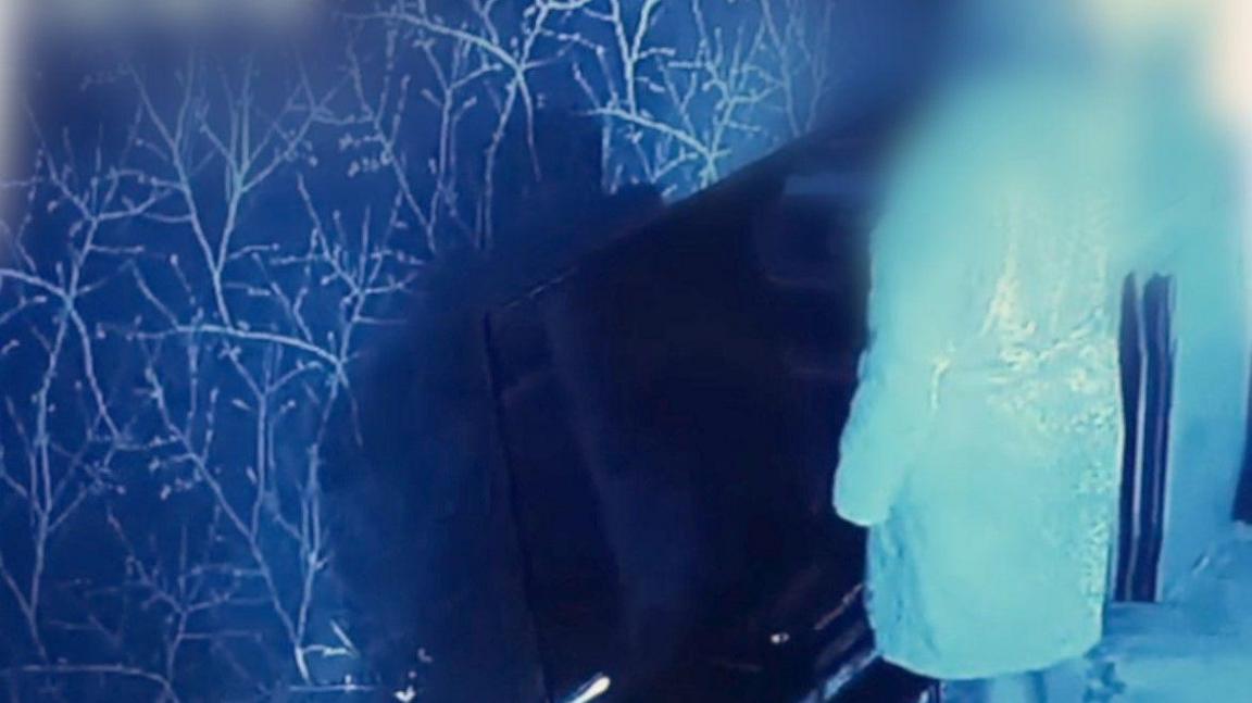 An inside wall that is blue and white. A woman whose face is not visible is standing in front of the wall that has a TV in front of it.