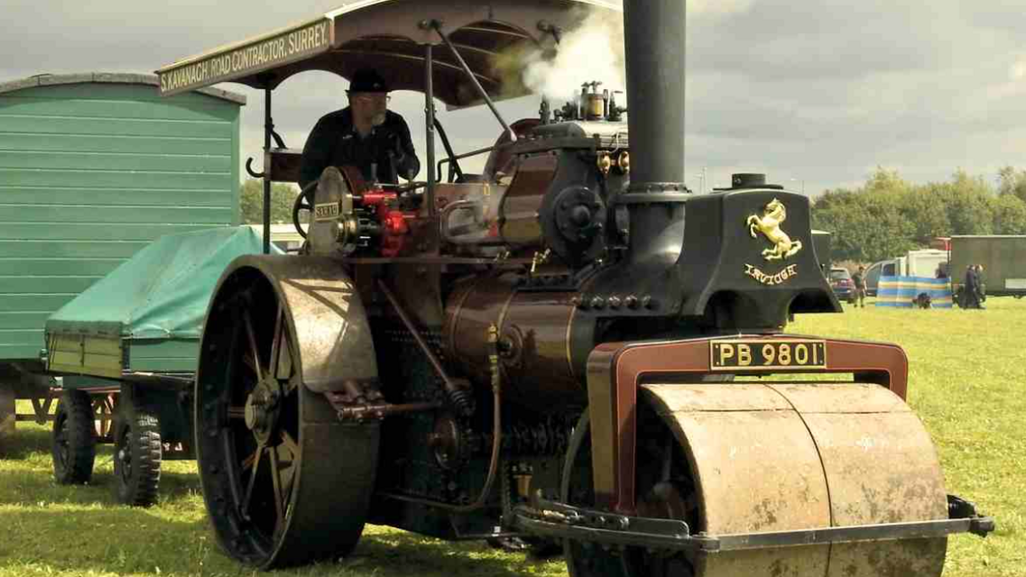 A man on a vintage-style brown and black tractor on grass