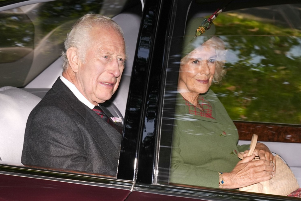 Charles and Camilla, who is wearing a green outfit and hat, in the back seat of a car looking out the window