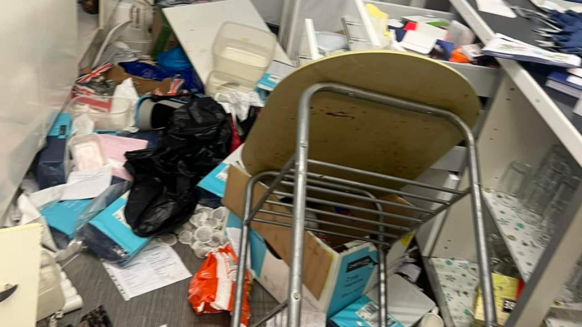 A table lies overturned on top of a box with paper, teabags and other equipment strewn across the floor 