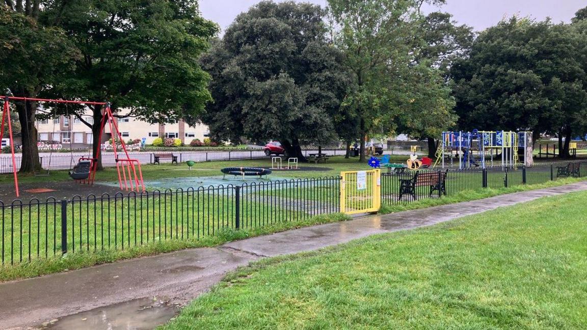 An empty park with colourful swings and a black metal fence with a yellow gate