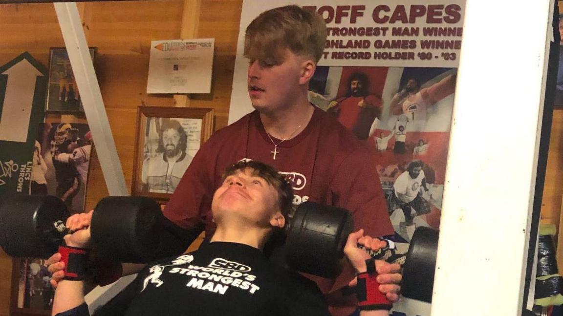 Lawson Capes lifts weights while older brother Donovan stands and spots him