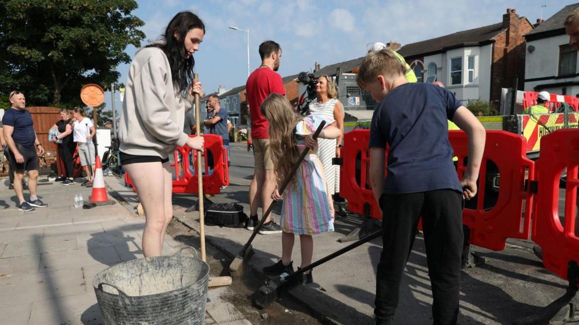 A teenage girl and young boy sweep the road 