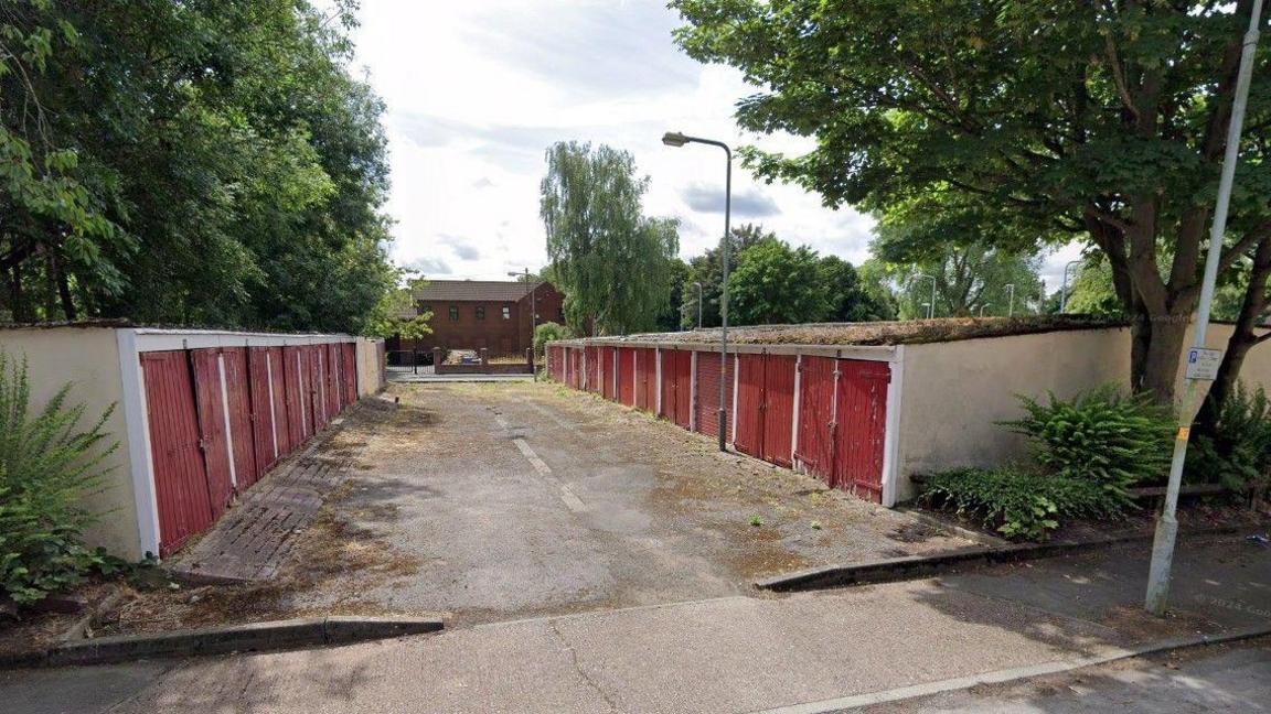 A street view image of two garage buildings with red doors