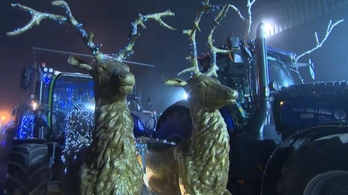 Two gold reindeer figures attached to a tractor as part of a Christmas parade display