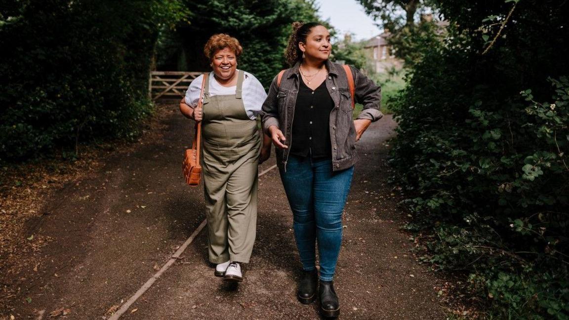 Two smiling women walking on a footpath through a wooded area