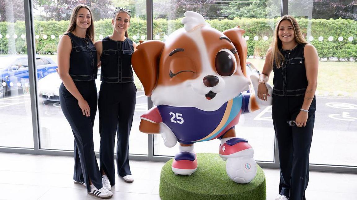 Poppy Soper (23, left), Olivia Clark (23, centre, left) and Safia Middleton-Patel (right, 20) pose with Euro 2025 mascot Maddli, an energetic Saint Bernard puppy named after Madeleine Boll (centre right).
