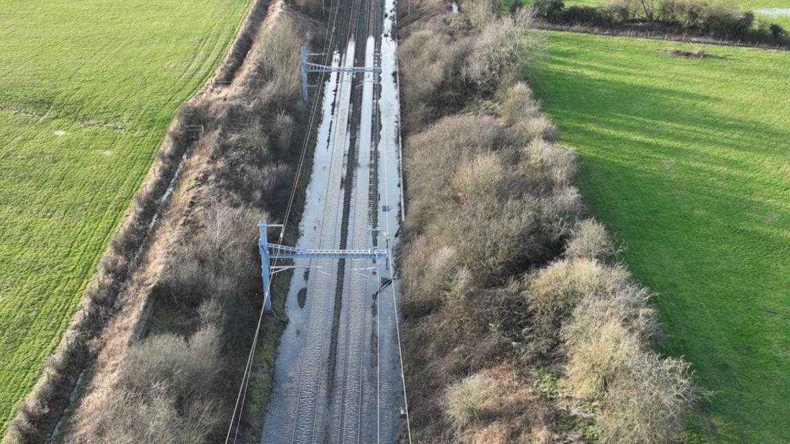 A drone shot of flooded railway tracks with bushes and fields either side.